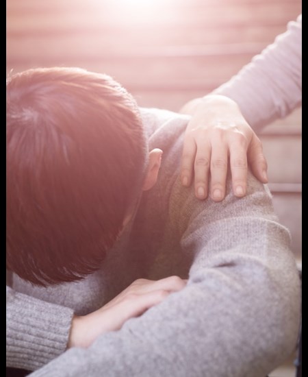 Boy with head on his knees and a girls hand on his shoulder