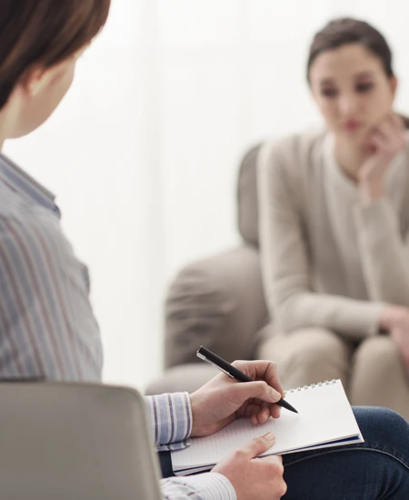 Psychiatrist taking notes while sitting with a patient.