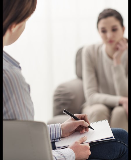 Psychiatrist taking notes while sitting with a patient.