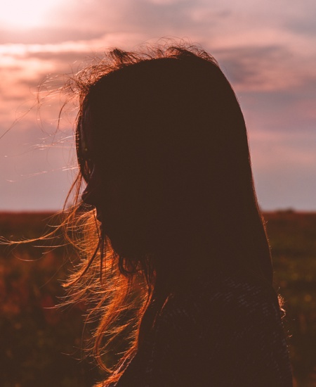 Profile of a girl with sunset in the background and hair blowing in the wind 