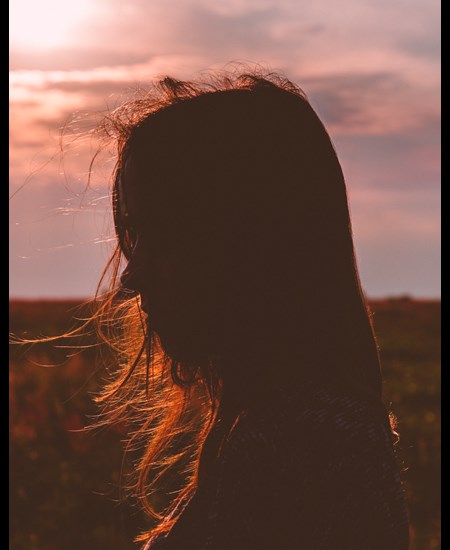 Profile of a girl with sunset in the background and hair blowing in the wind